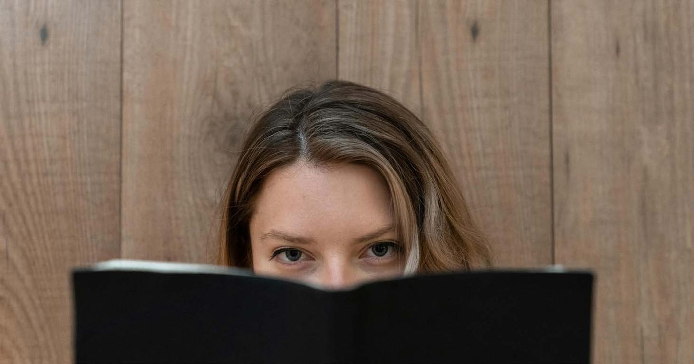 Junge Frau, die hinter einem aufgeschlagenen Buch hervorschaut
